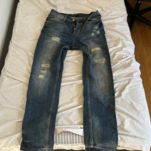 Exklusiva jeans från People's Uniform - Snygga unika blå jeans med slitna detaljer från People's Uniform. De har en klassisk femficksdesign och en cool, distressed look. Perfekta för en avslappnad stil. Passformen är Tapered. Pris kan diskuteras.