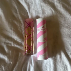 Pink Sugar Eau de Toilette - Säljer en söt och lekfull Pink Sugar Eau de Toilette. Flaskan är dekorerad med rosa och lila ränder och har en rosa kork. Förpackningen är vit med rosa spiralmönster. Perfekt för dig som älskar söta och ungdomliga dofter!