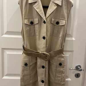 Beige väst med bälte - Snygg beige väst från Zara med knappar och bälte i midjan. Västen har flera fickor och en klassisk krage. Perfekt för att lägga till en stilren touch till din outfit.