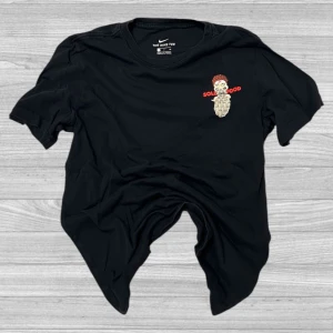 Nike T-Shirt - Säljer en svart t-shirt från Nike med ett coolt grafiskt tryck. Framsidan har en liten illustration med texten 'Sold Good' och baksidan visar en större illustration av en korvvagn med texten 'Los Zapatitos Más Frescos!'. Perfekt för dig som gillar unika och roliga tryck!