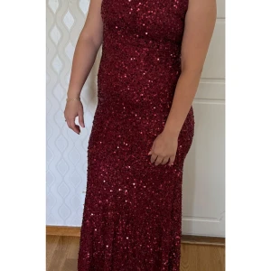 Vinröd paljettklänning - Snygg vinröd långklänning täckt med glittriga paljetter. Klänningen har smala axelband och en figurnära passform som framhäver silhuetten. Perfekt för en glamorös kväll!