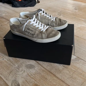 Saint Laurent skor  - Snygga beigea sneakers från Saint Laurent med vit sula och vit snörning.😊 Storlek 41 men passar nog 41-42! Perfekta för en avslappnad och trendig look. På hälen är skorna lite skadade men inget som märks! Skriv gärna om ni har några funderingar😁