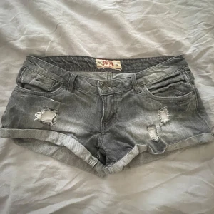 Lågmidjade jeansshorts - Snygga grå riktigt lowwaist jeansshorts med coola slitningar och upprullade kanter. De har en knapp och dragkedja framtill samt fickor både fram och bak. Ingen stretch. Står storlek 38 men skulle säga mer åt 34/36. Säljer endast då de sitter för tajt på mig då de inte har stretch, har vanligtvis 36. 
