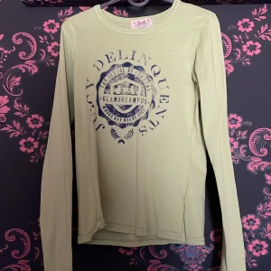  tröja från Juicy Couture - Säljer en grön långärmad tröja från Juicy Couture med ett tryck i blått på framsidan. Perfekt för en avslappnad stil med en touch av humor. Tröjan har en rund halsringning och är tillverkad i ett mjukt material. sitter mer som en s knappt använd
