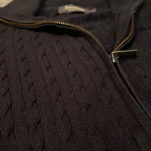 Svart stickad tröja från Dressmann - Säljer en stilren svart stickad tröja från Dressmann i herrstorlek S. Tröjan har en dragkedja framtill och ett klassiskt kabelstickat mönster. Den passar på S men sitter bättre på M. Tveka inte att göra av er om eventuella funderingar.