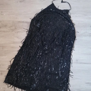 Svart glittrig klänning från Collection - Säljer en svart glittrig klänning från Collection. Klänningen har en elegant halterneck-design och är täckt med paljetter som ger en festlig look. Perfekt för en utekväll eller speciella tillfällen.