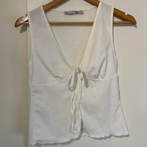 Vit topp  - Säljer en stilren vit ärmlös topp från 157. Toppen har en v-ringning och knytning framtill som ger en snygg detalj. Har sytt ihop själv under knytningen då den egentligen var helt öppen. Perfekt för varma dagar eller som ett lager under en jacka.