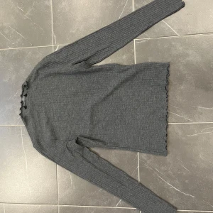 Grå ribbad tröja från ONLY - Säljer en stilren grå ribbad tröja från ONLY. Tröjan har långa ärmar och en fin volangdetalj vid ärmslut och nederkant. Perfekt för en avslappnad look.