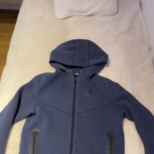 Nike tech new edition - Säljer en blå huvtröja från Nike med dragkedja och två praktiska fickor framtill. Tröjan har en stilren design med Nike-logga på bröstet och är perfekt för en avslappnad stil. Och inga fläckar