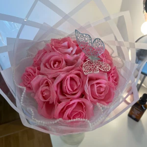 Bukett med rosa rosor och fjärilsdekoration - Vacker bukett med rosa rosor inslagna i transparent papper. Dekorerad med en elegant silverfärgad fjäril. Perfekt som present eller dekoration.