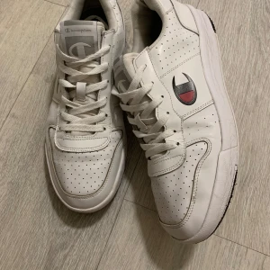 Vita sneakers från Champion - Snygga vita sneakers från Champion med perforerade detaljer och klassisk snörning. Skorna har en diskret logga på sidan och är perfekta för en stilren look.