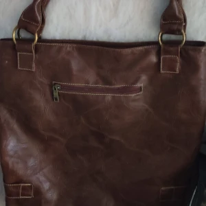 Brun skinnväska från D&G - Snygg brun skinnväska från D&G med stilrena detaljer. Väskan har metallspännen och en praktisk dragkedja på baksidan. Perfekt för att bära med sig det viktigaste med stil.