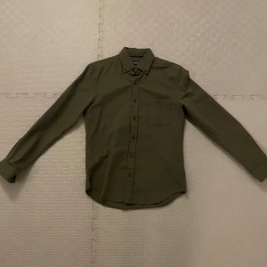 Grön skjorta dressman - Säljer en lite mörk grön skjorta från dressman som är för liten för mig, den är i storleken small och sitter lite mer slimmad så inte så pösigt köpte den nån gång förra året men har inte kommit så mycket till användning för den blev för liten rätt så snabbt. De är bara att höra av sig vid minsta lilla 