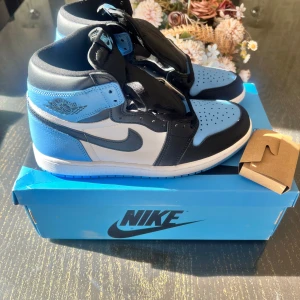 Jordan 1 High unc  - Snygga Nike Air Jordans i en fräsch kombination av blått, svart och vitt. Är i perfekt skick då de aldrig använts. Det ingår svarta och blå snören 