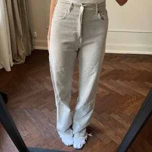 Grå jeansbyxor från Zara - Snygga grå jeansbyxor från Zara med hög midja och raka ben. Byxorna har en klassisk femficksdesign och stängs med dragkedja och knapp. Perfekta för en stilren look.