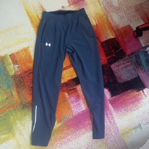 Mörkblå träningsbyxor från Under Armour - Säljer ett par mörkblå träningsbyxor från Under Armour med en praktisk speedpocket. Byxorna har en normal passform och är perfekta för löpning eller gymmet. De har en elastisk midja och en liten logga på benet.