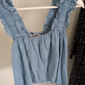 Blå topp med volang från Hampton Republic - Säljer en söt blå topp från Hampton Republic i storlek XS. Toppen har volangdetaljer längs axlarna och en luftig passform. Perfekt för varma dagar och ger en romantisk touch till din outfit. 💙