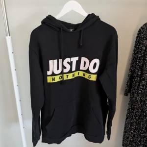 Svart hoodie från FSBN - Säljer en svart hoodie från FSBN med texten 'JUST DO NOTHING' i vitt och gult på framsidan. Tröjan har en klassisk design med huva och dragsko samt en stor magficka. Perfekt för en avslappnad stil.