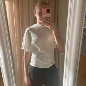 Vit ribbad topp - Säljer en stilren vit ribbad topp med korta ärmar. Toppen har en bekväm passform och är perfekt för både vardag och festliga tillfällen. Den är tillverkad i ett mjukt och stretchigt material som ger en skön känsla hela dagen.