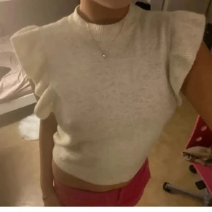 Vit stickad topp med volangärmar - Köpte för 499kr Säljer en söt vit stickad topp med volangdetaljer på ärmarna. Toppen är croppad och har en rund halsringning. Perfekt för en stilren och trendig look.