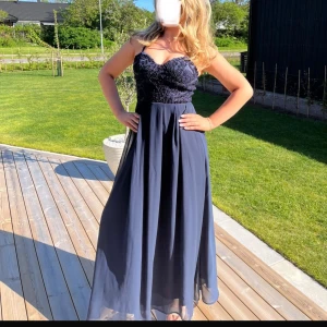 Mörkblå långklänning från AX Paris - Elegant mörkblå långklänning från AX Paris med vackert broderat liv och hjärtformad urringning. Klänningen har smala axelband och ett flytande kjolparti som ger en fin siluett. Perfekt för speciella tillfällen.