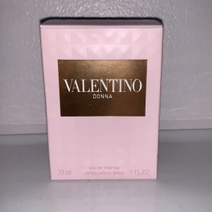 Valentino Donna Eau de Parfum - Helt ny, oöppnad. Elegant och feminin parfym från Valentino i en stilren rosa förpackning. Innehåller 30 ml av den klassiska doften Donna, perfekt för den som vill ha en sofistikerad och tidlös doftupplevelse. Förpackningen har en lyxig känsla med guldiga detaljer.