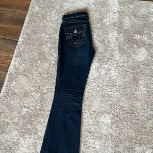  True religion becca mörkblåa bootcut  - Snygga mörkblå bootcut jeans med dekorativa bakfickor och kontrastsömmar. Jeansen har en klassisk femficksdesign och stängs med dragkedja och knapp. Perfekta för en avslappnad stil.