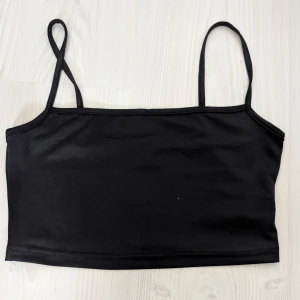 Svart tubtopp med smala axelband - Snygg svart tubtopp med smala axelband. Perfekt för en stilren look. Enkel och mångsidig topp som passar till det mesta.