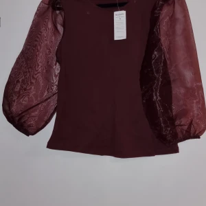 Vinröd topp med puffärmar, st S - Snygg vinröd topp från Bik Bok med unika puffärmar i ett transparent material. Perfekt för att ge en elegant touch till din outfit. Toppen har en normal passform och är tillverkad i ett mjukt tyg.