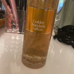 Golden Mandarin Saffron Fragrance Mist - En lyxig doftmist från Victoria's Secret med noter av gyllene mandarin och saffran. Flaskan rymmer 250 ml och har en elegant design med gyllene detaljer. Perfekt för att ge en fräsch och exotisk doft.