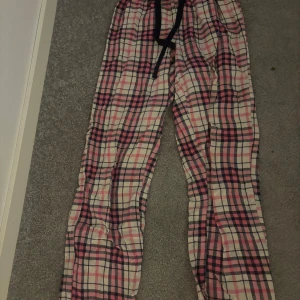 Pyjamas byxor - Säljer ett par mysiga rutiga byxor i rosa och vit med snörning i midjan. Perfekta för en avslappnad dag hemma. Byxorna har en loose passform och är tillverkade i ett mjukt material. Dom är i storlek xs/s.