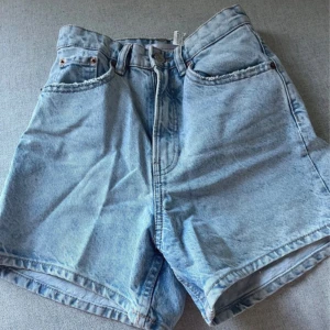 Ljusblå jeansshorts - Säljer ett par ljusblå jeansshorts med klassisk femficksdesign. De har en hög midja och stängs med dragkedja och knapp. Perfekta för sommardagar! Pris kan diskuteras och jag är villig till att sänka priset!!!