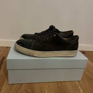 Lanvin skor - Snygga mörk gråa sneakers från Lanvin med en stilren look. Har använts en del men har fortfarande mycket kvar att ge. Både original låda och dust bag finns med. Dem har ett märke på vardera sko på cap toen se bild 2. Men annars i bra skick.