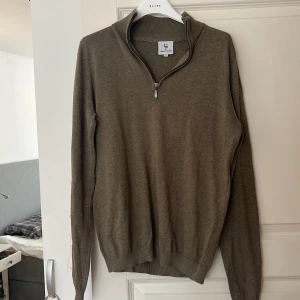 Olivgrön tröja från Urban Pioneers - Säljer en olivgrön tröja från Urban Pioneers i storlek S. Tröjan har en dragkedja vid halsen och är tillverkad av 50% bambuviskos och 50% bomull. Perfekt för en stilren och bekväm look.