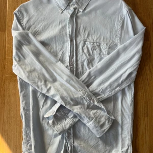 Ljusblå skjorta från Filippa K - Säljer en stilren ljusblå skjorta från Filippa K. Skjortan har en klassisk krage och knappar framtill. Perfekt för en avslappnad men ändå elegant look.