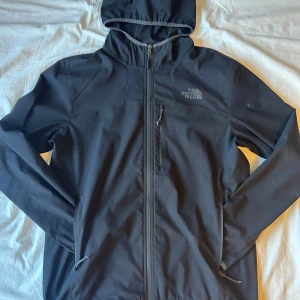 Svart jacka från The North Face - Säljer en svart jacka från The North Face med huva och dragkedja. Jackan har en stilren design med en bröstficka och är perfekt nu inför våren. Passar bra till både jeans och träningskläder.