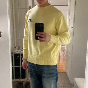 Mjuk Gul tröja från J.Lindeberg - Säljer en snygg gul tröja från J.Lindeberg med ett stilrent svart logotypbroderi på bröstet. Tröjan har långa ärmar och ribbade muddar vid ärmslut och nederkant. Perfekt för en avslappnad stil.