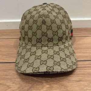 Beige keps från Gucci - Snygg beige keps från Gucci med det ikoniska GG-mönstret. Kepsen har en justerbar rem baktill och är perfekt för att ge en lyxig touch till din outfit. Passar både till vardag och speciella tillfällen.