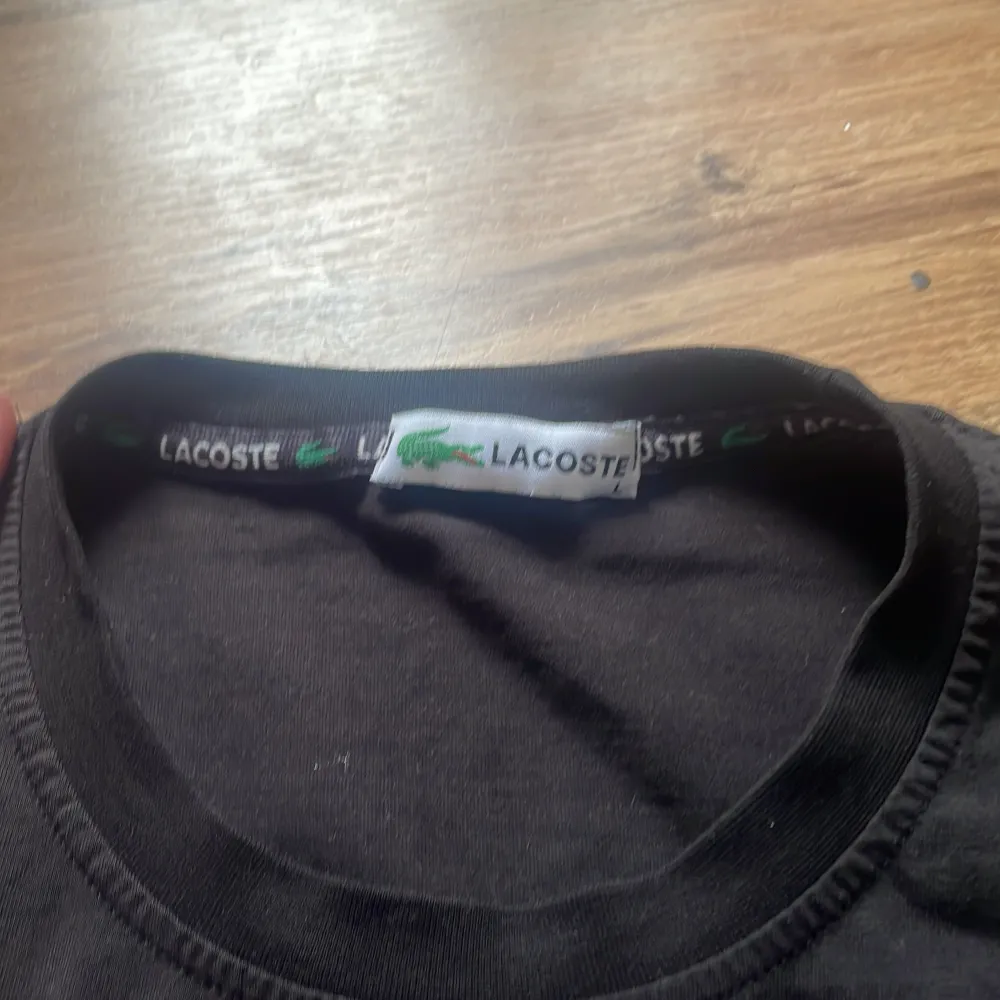 Säljer en klassisk svart t-shirt från Lacoste med den ikoniska krokodilloggan på bröstet. T-shirten har en rund halsringning och korta ärmar. Perfekt för en stilren och avslappnad look.. T-paidat.