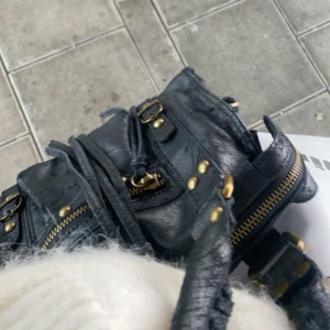 Svart handväska  - Snygg svart handväska med guldfärgade detaljer och dragkedjor. Såå snygg och rymlig!! Köpt förra sommaren i Italien. Väskan har ett stort fack med två mindre varav ett har dragkedja. Remmarna går att knyta lös. Inte så mycket använd, ser inga defekter. Pris kan diskuteras, kom med prisförslag💞❤️