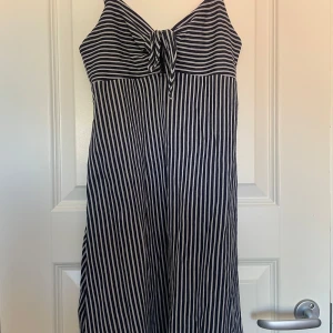 Randig klänning från Gina Tricot - Kort randig klänning i mörkblått och vittmed knytning fram. Perfekt för varma sommardagar. Endast använd ett fåtal gånger.