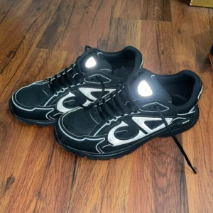 Svarta sneakers från Dior B30 - Snygga svarta sneakers från Dior med vita detaljer och snörning. Skorna har en robust sula och en stilren design som passar perfekt för en modern look.       Storlek 41, använda en gång. Skorna reflekterar. Inget kvitto.