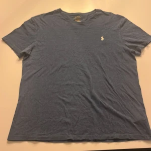 Blå t-shirt från Ralph Lauren - Säljer en snygg blå t-shirt från Ralph Lauren med det klassiska broderade logotypen på bröstet. T-shirten är kortärmad och gjord i mjuk bomull, perfekt för en avslappnad stil. Passar bra till jeans eller shorts för en cool look. 🌟