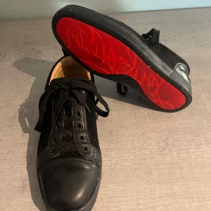 Svarta loubtins - Snygga svarta sneakers från Christian Louboutin med den ikoniska röda sulan. Skorna har snörning och en rund tå, vilket ger en klassisk look. Perfekta för dig som vill ha en stilren och lyxig touch i vardagen.