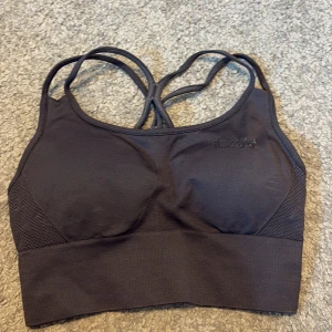 Mörkgrå sporttopp från ICANIWILL - Säljer en mörkgrå sporttopp från ICANIWILL med korsade axelband och meshdetaljer på sidorna. Toppen har en tight passform. Den har vaddering så man behöver inte ha en bh under denna. Är i storlek XS. Endast provad, aldrig använd efter. 