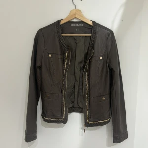 Brun skinnjacka från Ciao Milano - Snygg brun skinnjacka från Ciao Milano med flätade detaljer vid kragen och guldfärgad kedja längs kanterna. Jättefin på en sommarkväll!💕Den har några täcken på användning men enligt mig är det inget som förstör. Hör av dig vid frågor!