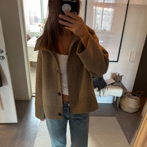 Beige kappa - Säljer en stilren beige kappa med knappar framtill. Jackan har en normal passform och långa ärmar, perfekt för höst och vår. En tidlös design som passar till många olika outfits.