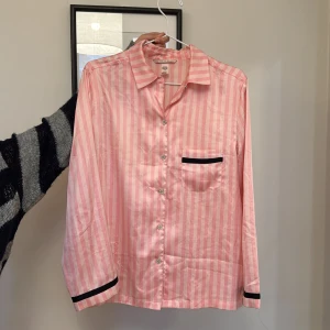 Rosa randig pyjamas från Victoria's Secret - Pyjamas skjorta från Victoria secret. Den är i ett jättefint skick, det ända är en liten fläck som man kan se på sista bilden. Har dock inte testat att tvätta bort den så den kan kanske försvinna, därmed säljer jag den billigt! 💕