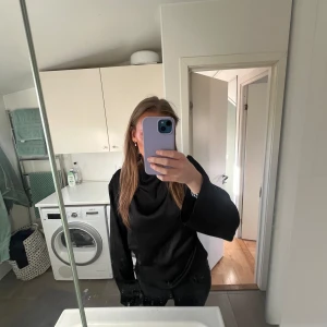 Svart långärmad topp - Säljer en elegant svart topp med långa ärmar. Perfekt för en stilren look. Toppen har en hög krage och är i satin.