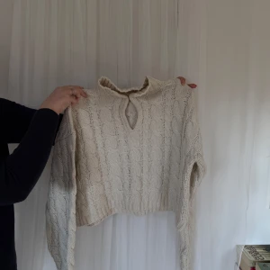 Beige stickad tröja med knyt - Säljer en mysig beige stickad tröja med ett knyt vid halsen. Tröjan har ett fint kabelstickat mönster och långa ärmar. Perfekt för kyliga dagar!